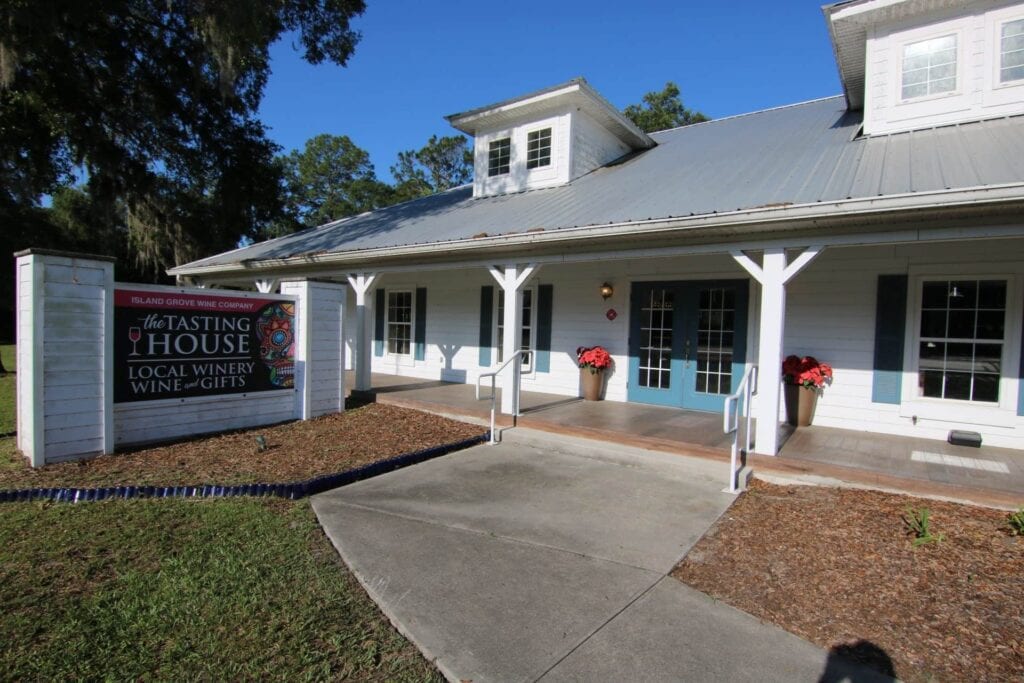 The exterior of The Tasting House with white siding, a metal roof, and blue French doors