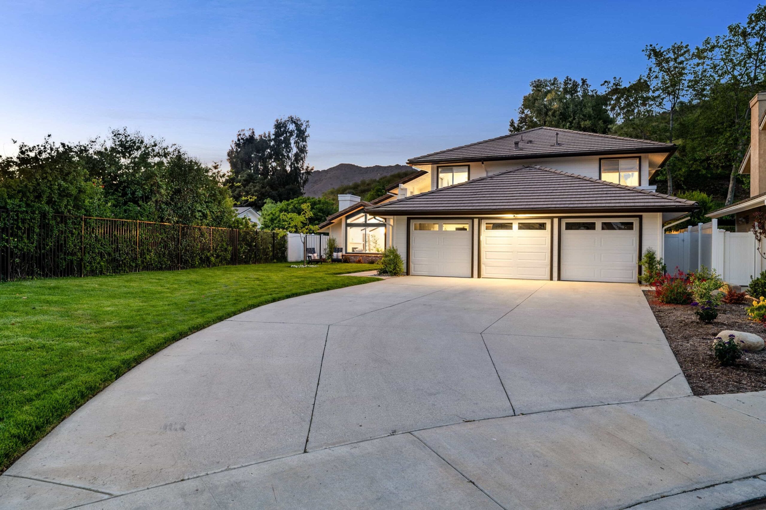A modern two-story white suburban home featuring a spacious three-car garage and a wide concrete driveway at twilight, showcasing high-end real estate in Calabasas, CA.